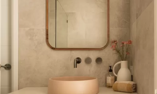 Modern bathroom with wooden vanity, beige round sink, large mirror, and decorative flowers in a vase