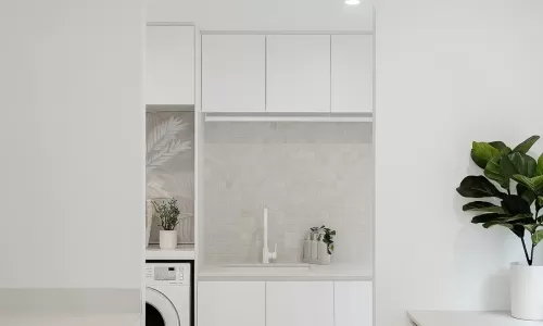 A minimalist laundry room with white cabinets, a washing machine, and a plant on the counter
