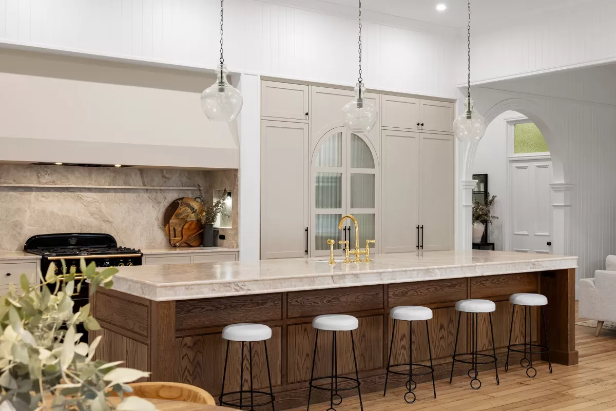 Dark wooden kitchen island with white countertop, gold faucet, and five white bar stools.