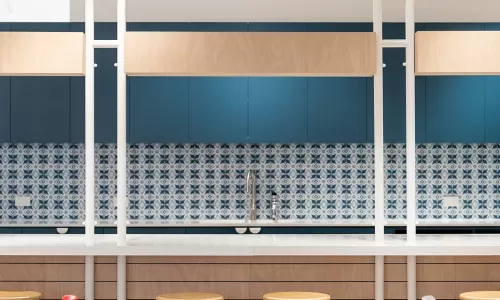 Colorful kitchen space with patterned blue backsplash, wood paneling, bar stools, and red-accented chairs.