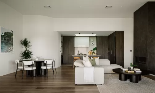 Open living area with light furniture, dark wood kitchen, round dining table, and fireplace.