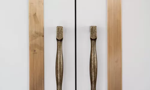 Close-up of white cabinet doors with brass trim and antique-style brass handles in a modern kitchen