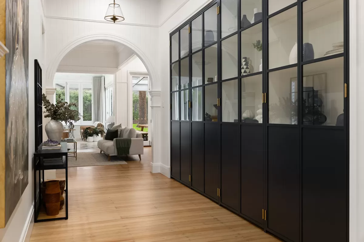 Foyer with black framed glass cabinet doors, a large archway, and wood floors.