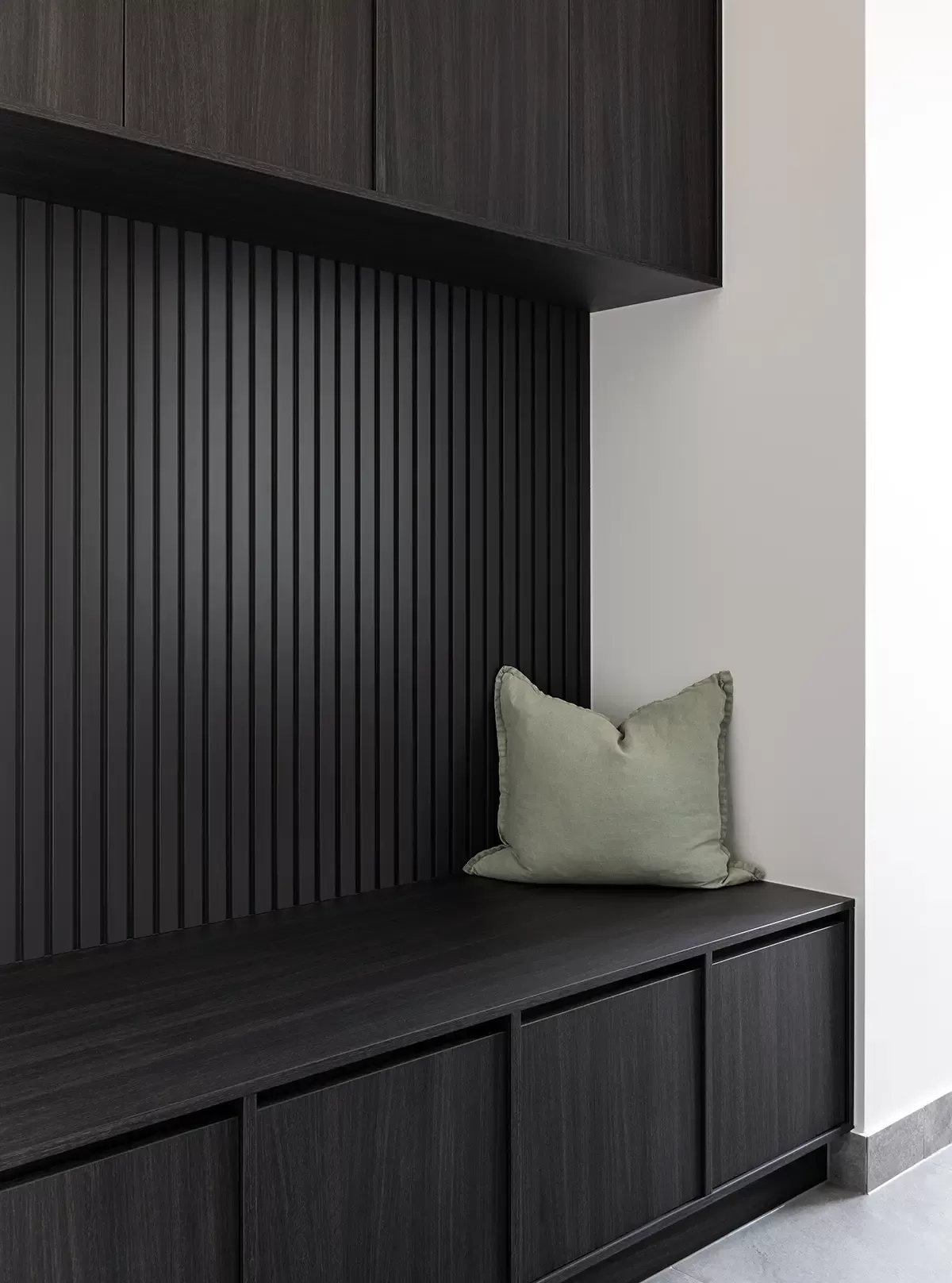 A modern mudroom with dark wood cabinetry, a black slatted wall, and a green cushion on the bench