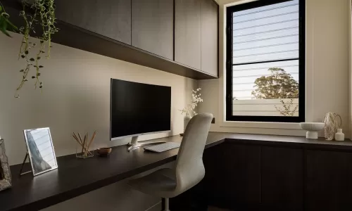 Minimalist home office with dark wood cabinetry, monitor setup, and large window view.