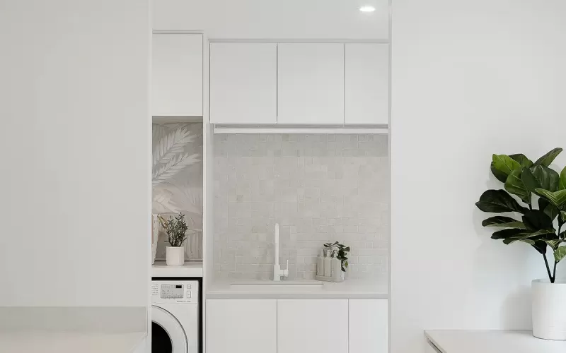 A modern and minimalistic laundry room interior with white cabinets, and a washing machine