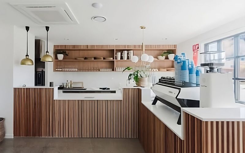 Minimalist cafe counter with vertical wood slats, white countertop, and espresso machine.