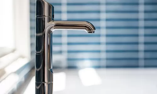 Close-up of a modern chrome tap on a speckled countertop, with glossy blue tile backsplash in background.