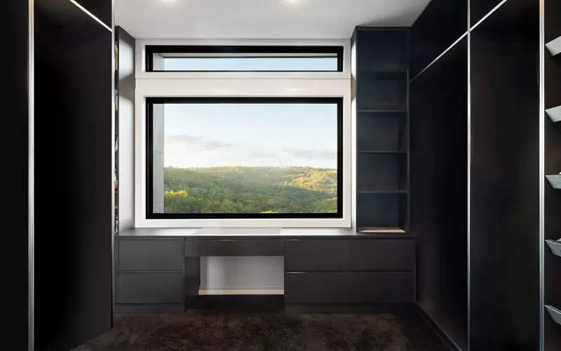 Modern closet design with built-in drawers and shelves framing a large window with a view of a green forest landscape
