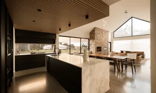 Open-concept kitchen and living room with marble island, stone fireplace, vaulted ceiling, and large windows