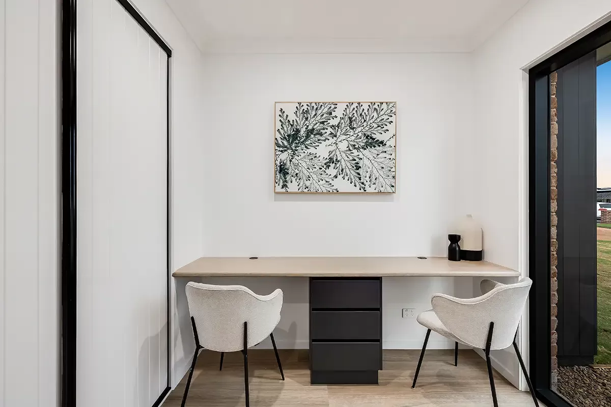 A minimalist study room with a wooden desk, black drawers, and two beige chairs